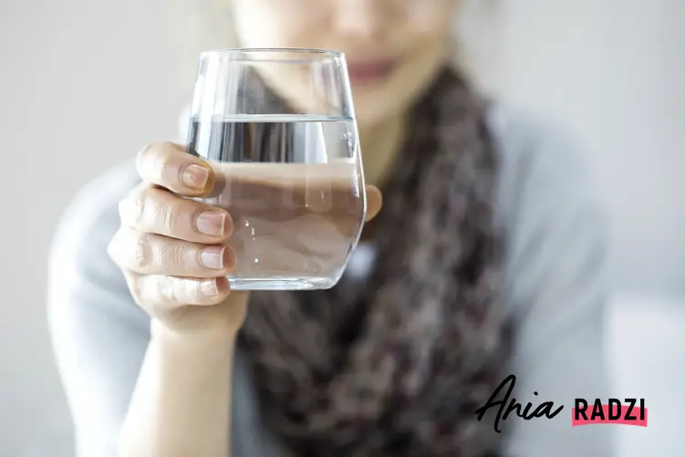 Kobieta trzymająca szklankę wody oraz najlepsze sposoby, jak pozbyć się wody z organizmu
