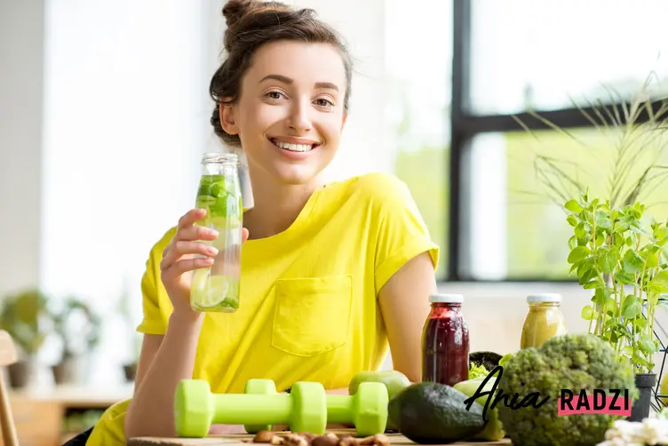 Uśmiechnięta kobieta w zółtej koszulce pijąca wodę z dodatkami i porady, jak oczyścić organizm z toksyn
