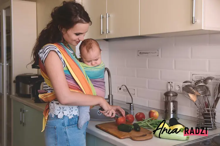 Kobieta z dzieckiem w chuście podczas krojenia owoców, a także informacja, jakie owoce można jeść podczas karmienia piersią