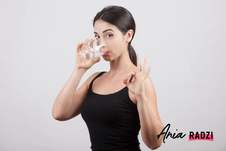 Kobieta trzymająca przy ustach szklankę wody, a także porady, na co pomaga płukanie gardła sodą