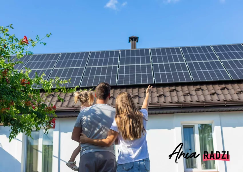 rodzina stoi przed domem z panelami PV na dachu