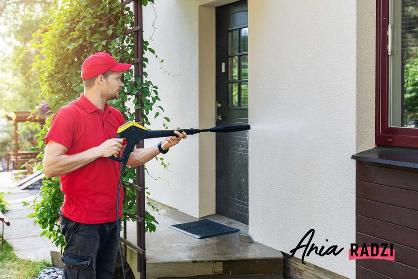 Mężczyzna myjący elewację przy drzwiach za pomocą myjki ciśnieniowej, a także informacje, jak i czym wyczyścić dokładnie elewację domu