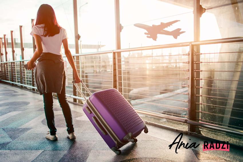 Kobieta z walizką na lotnisku, a także aktualny ranking najpopularniejszych walizek do samolotu