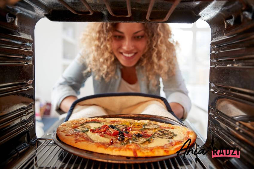 Kobieta wkładająca pizzę do piekarnika, a także porady, w jakiej temperaturze piec pizzę