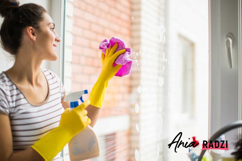 Kobieta podczas mycia okien oraz podpowiedzi, czym myć okna krok po kroku, najlepsze preparaty do mycia okien